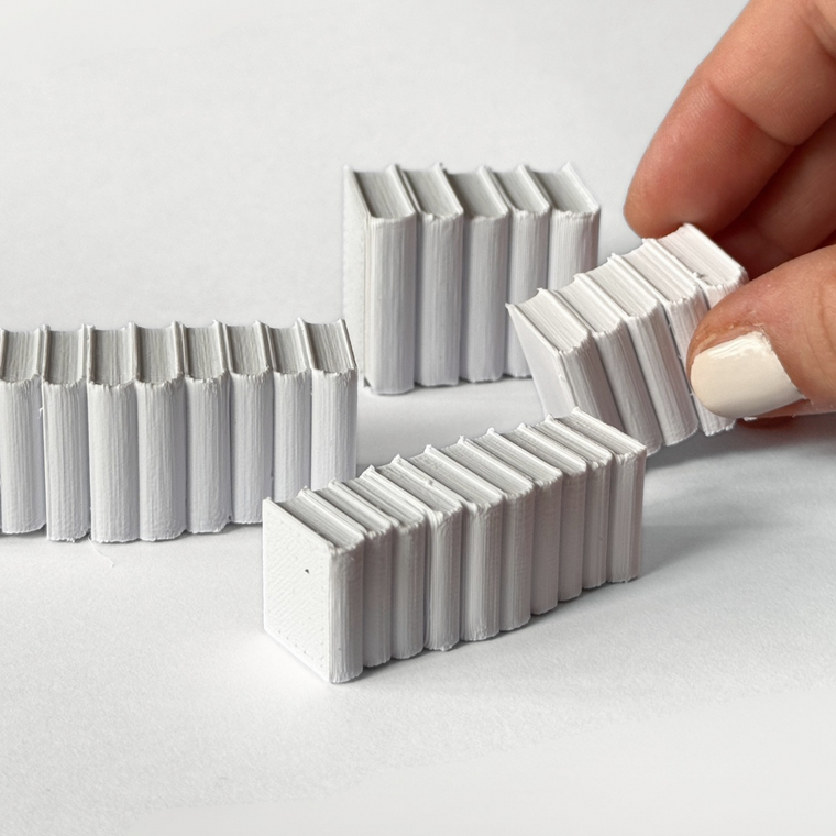 Witte 3D-geprinte rijtjes miniatuurboeken, een hand pakt er een rij op, door Miniatures Guild