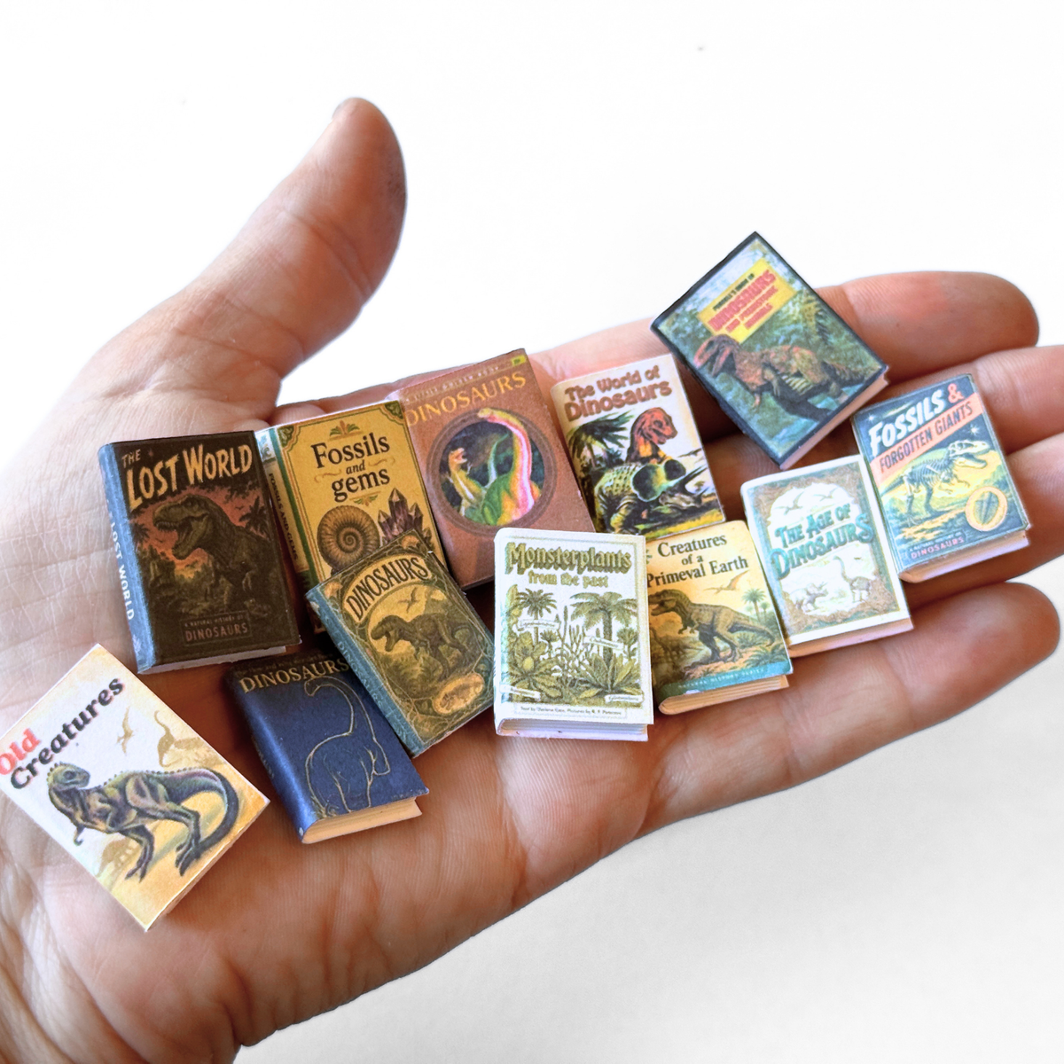 Miniatuurboekjes met printbare dinosaurusboekomslagen op een hand, schaal 1:12, door Miniatures Guild