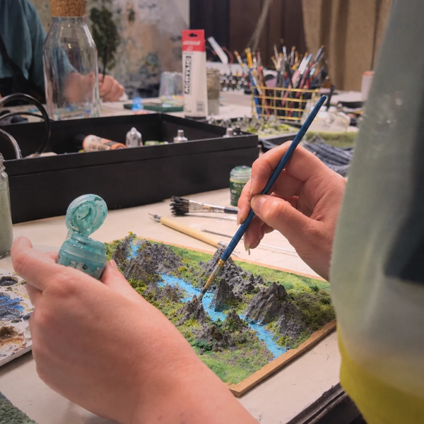Deelnemer schildert een miniatuurlandschap met rivier en bomen tijdens de Miniature Landscape workshop van Miniatures Guild in Utrecht