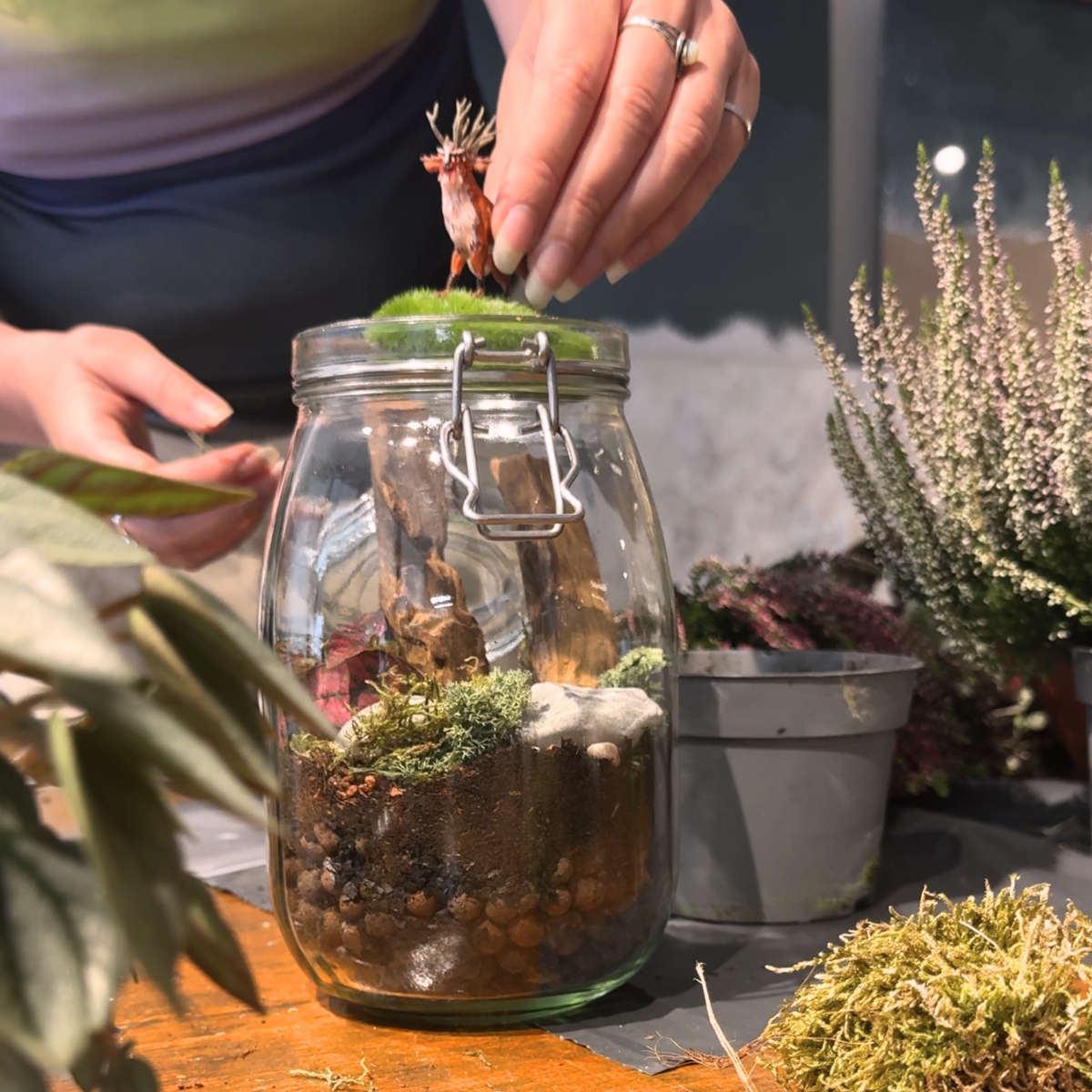 Hand plaatst een figuurtje op het mos tijdens de terrarium workshop, door Miniatures Guild